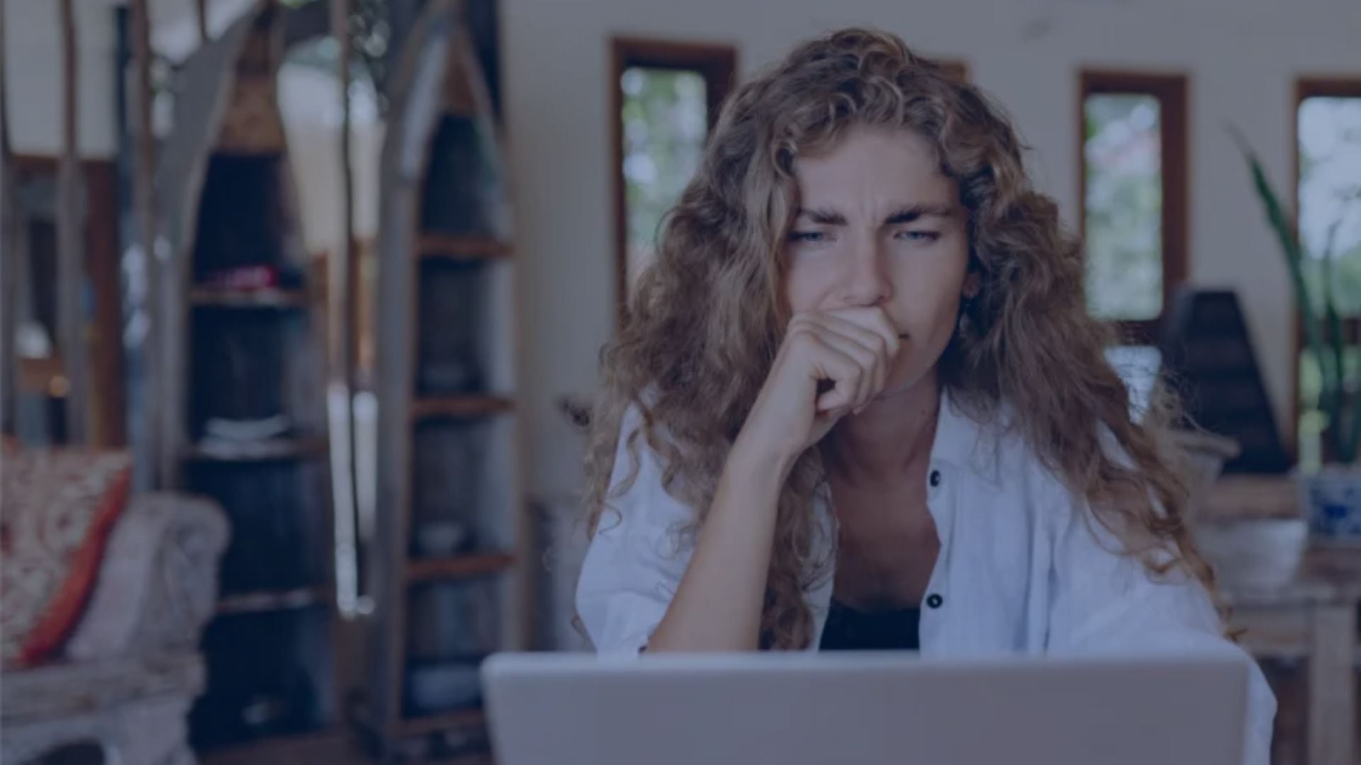 A woman sitting at a table with her laptop, frustrated while learning Finnish and preparing for the YKI test.
