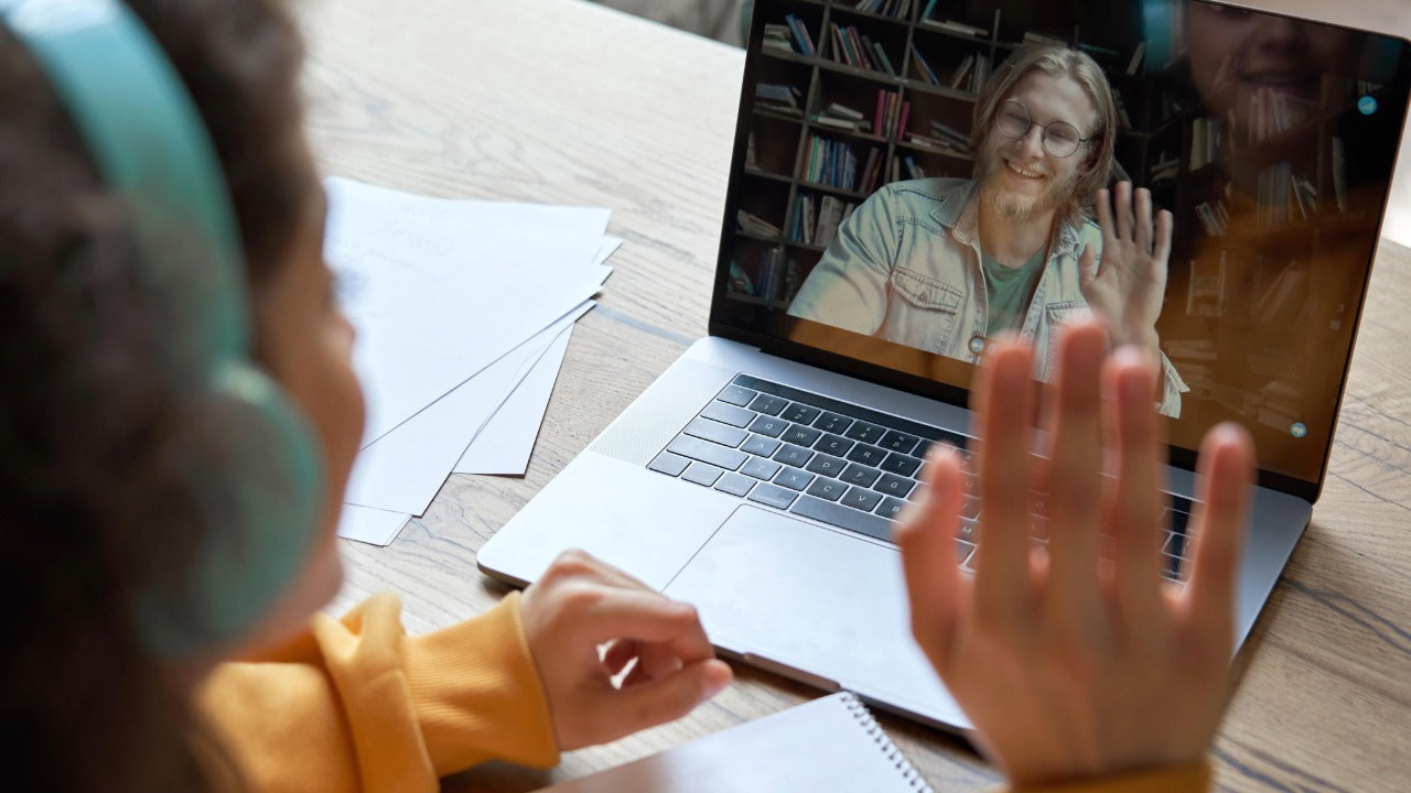 Finnish teacher waving from laptop in YKI lesson.