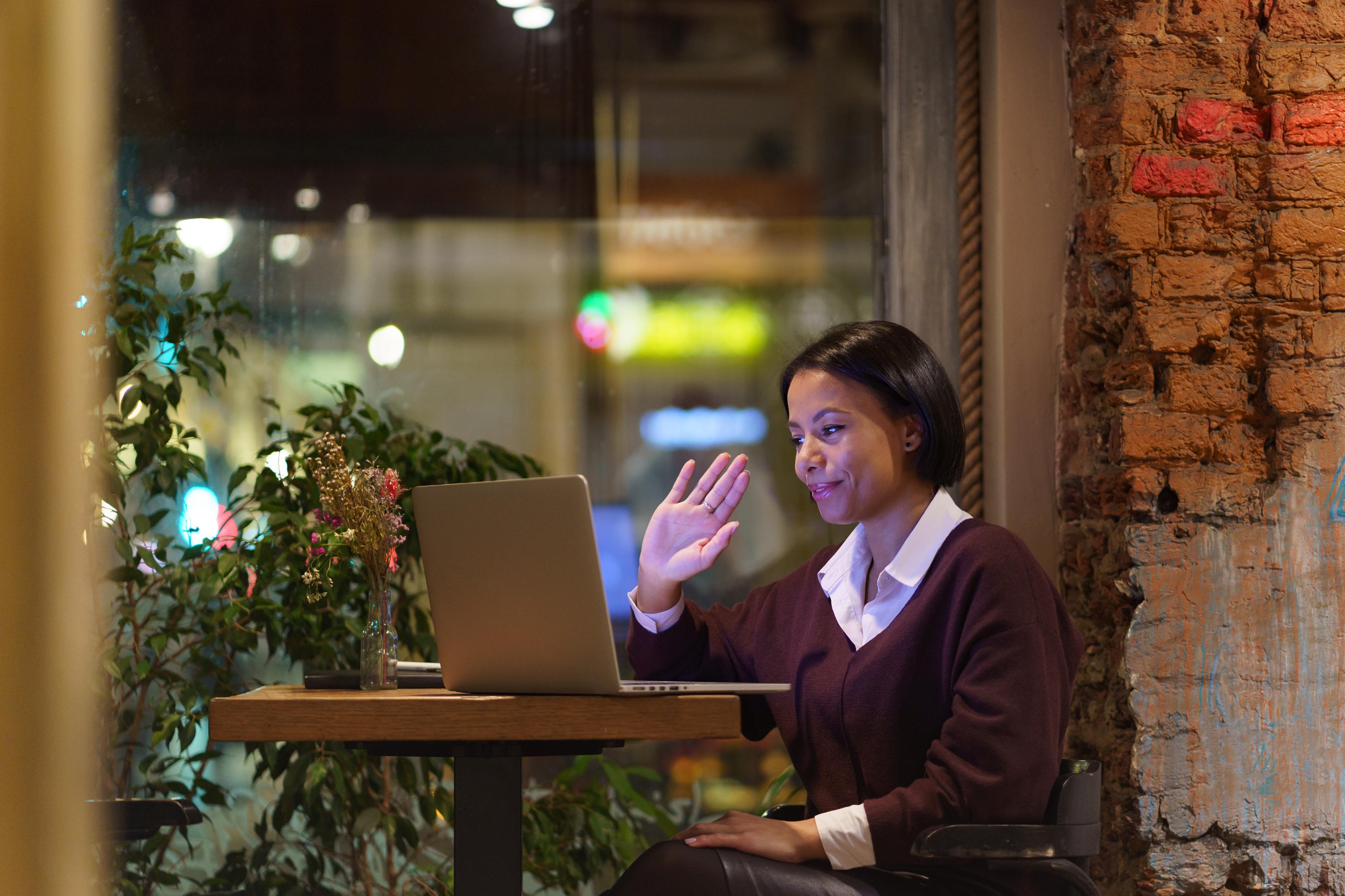 Young friendly afro American woman waving in a online lesson sitting in a cafe.