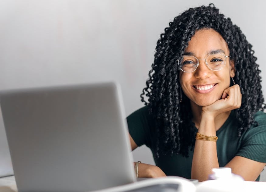 A smiley woman with curly hair sitting at a desk with a laptop.