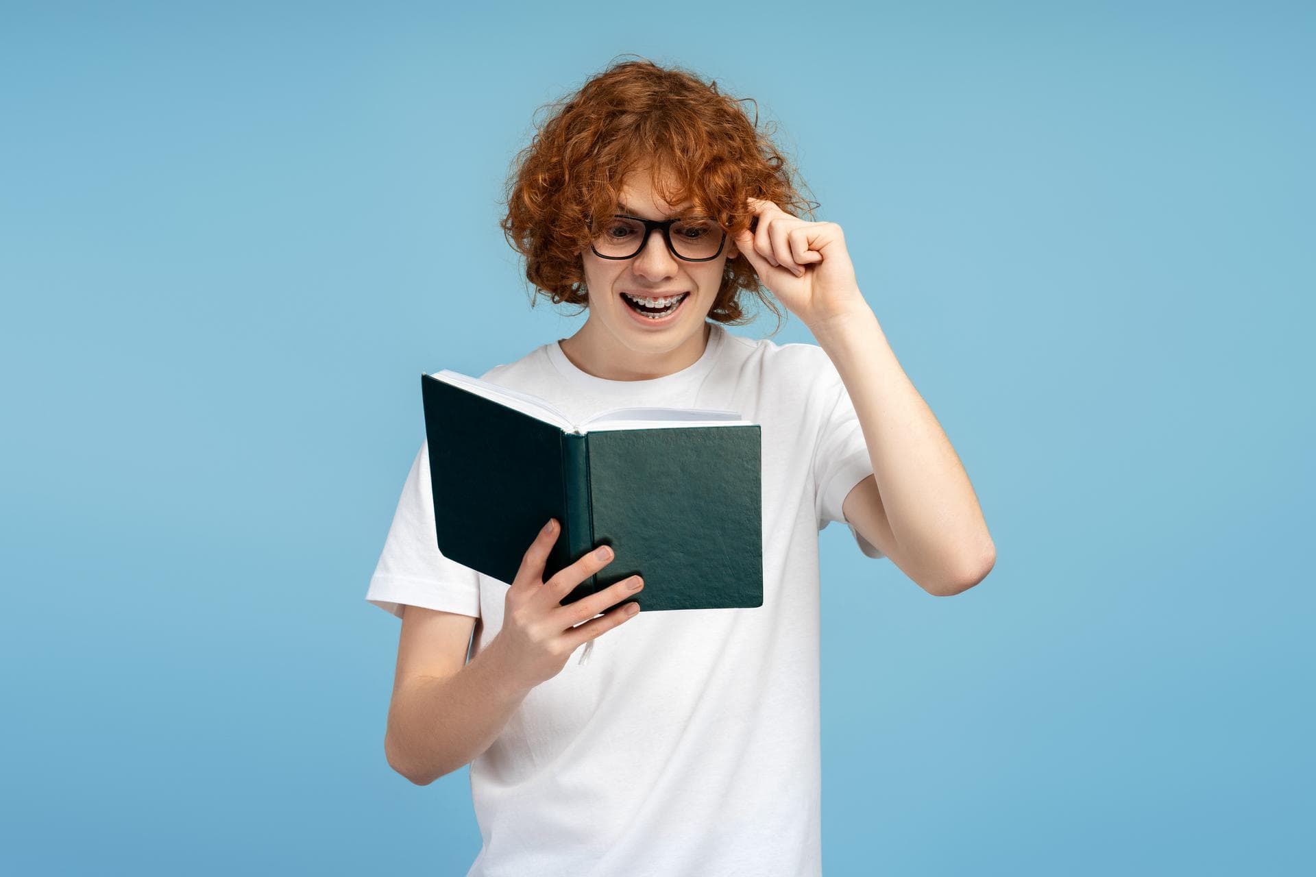 Man with red hair and glasses holding a book, focusing on learning Finnish for YKI test.