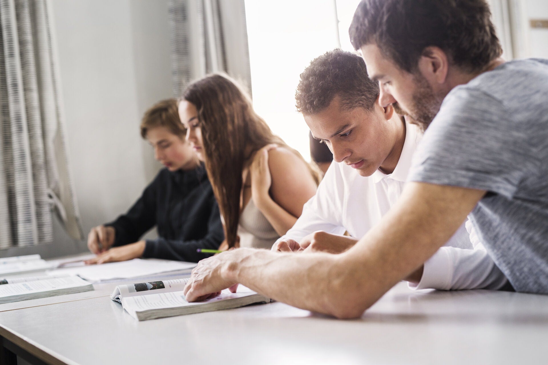 Four people sitting at a table surrounded by papers and documents are preparing for the YKI test. 